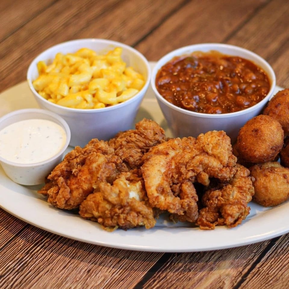 A plate of fried chicken, hush puppies, mac and cheese, baked beans, and ranch dressing.